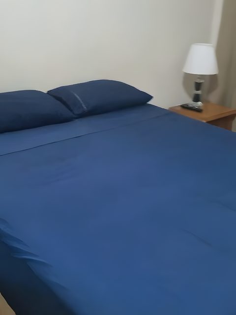 A cama de casal do Quarto 4, com roupa de cama azul e abajur na cabeceira.
